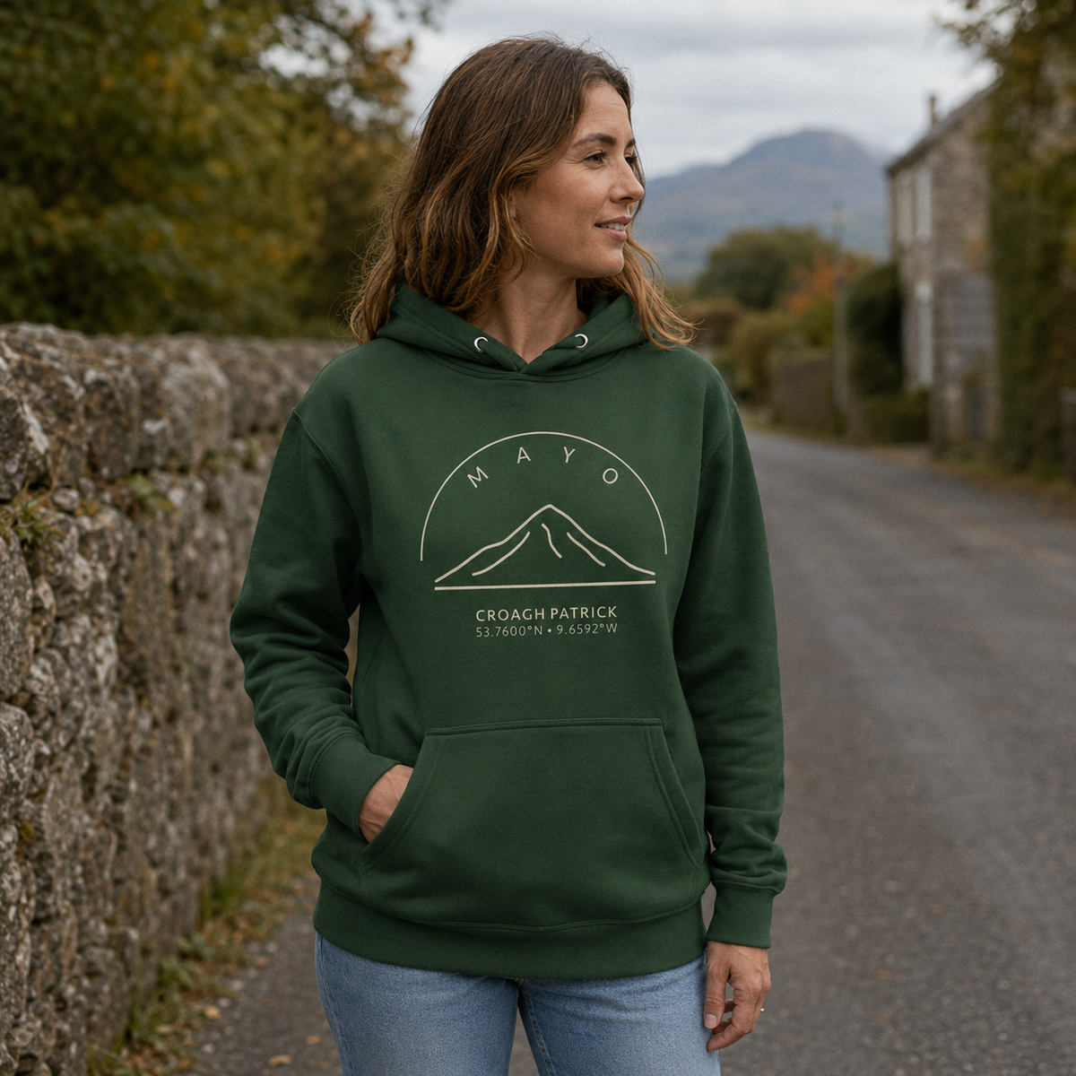 A woman wearing a dark green hoodie with a white mountain graphic and the text 'MAYO CROAGH PATRICK' stands on a stone path outdoors.